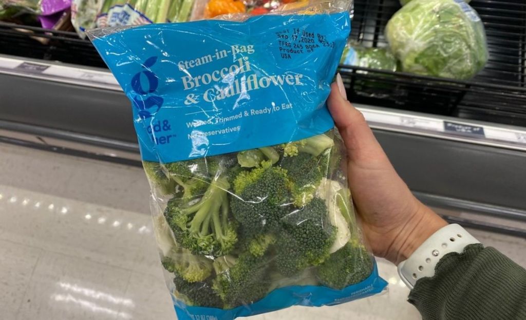 A hand holding a bag of broccoli and cauliflower at a store