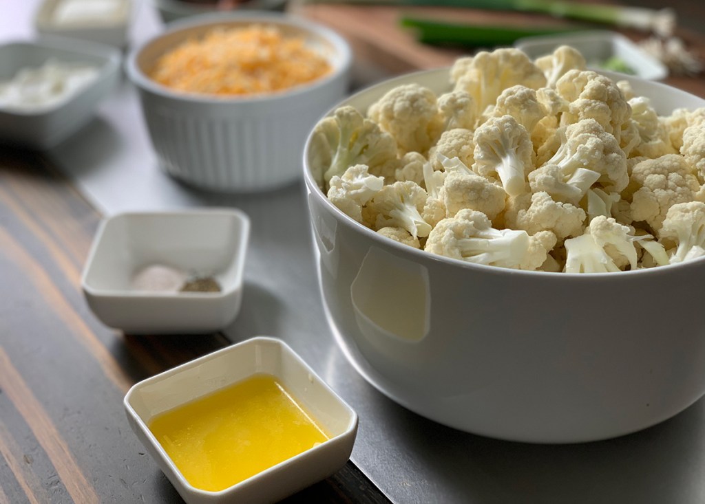 bowl of cauliflower, melted butter, seasonings, and cheese