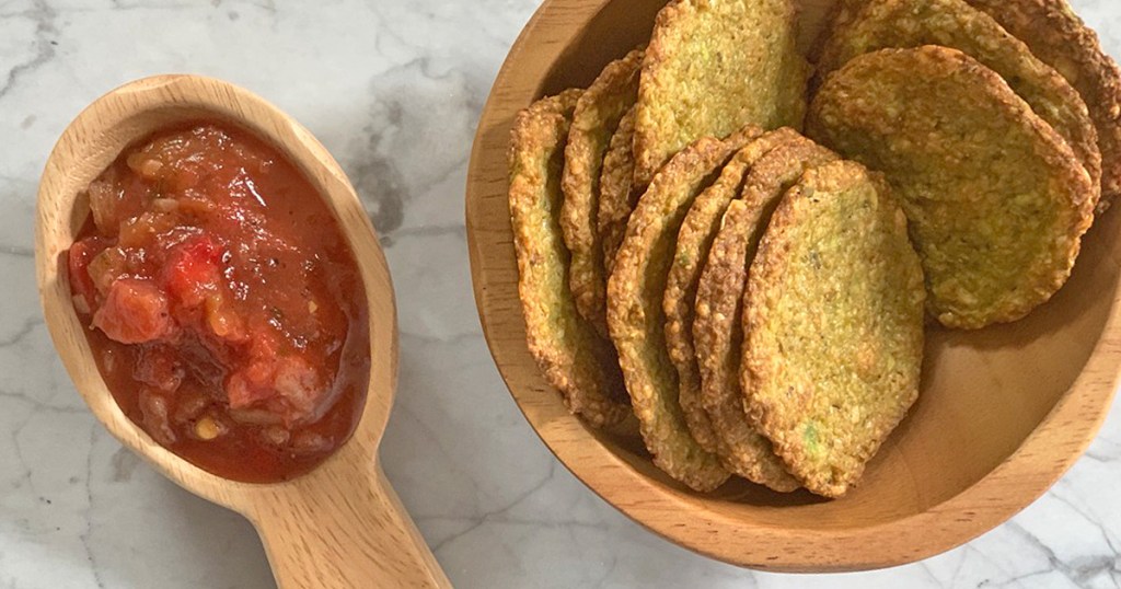 a wooden bowl of avocado chips next to a bowl of salsa
