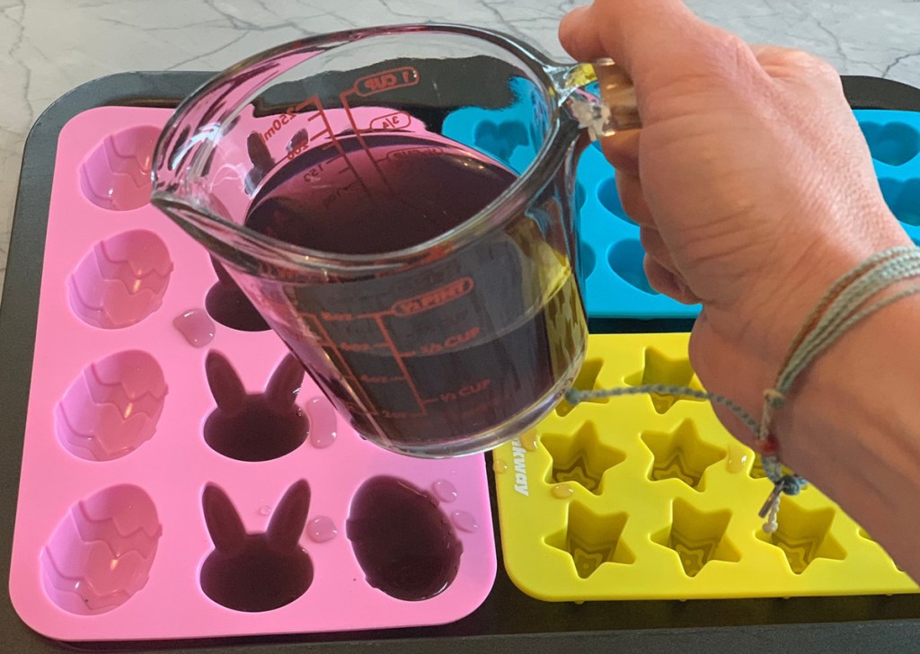 hand pouring jello mixture into molds