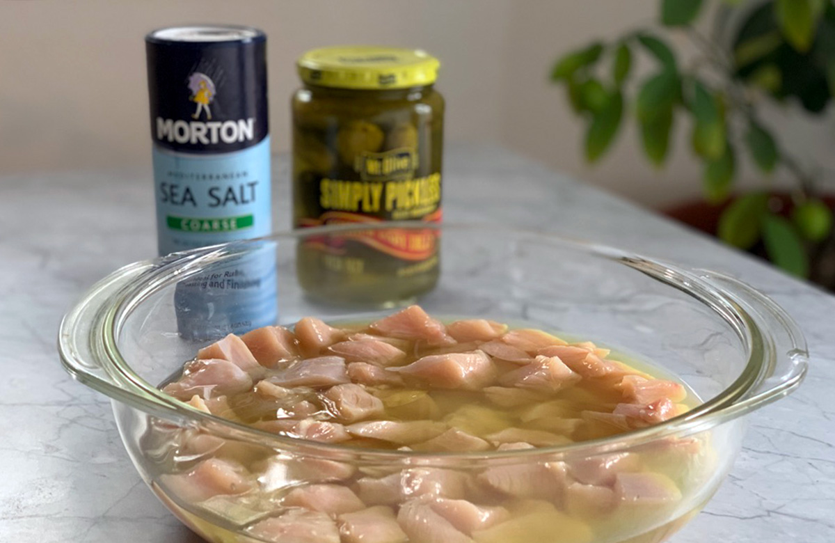 a glass bowl filled with chicken soaking in a pickle brine