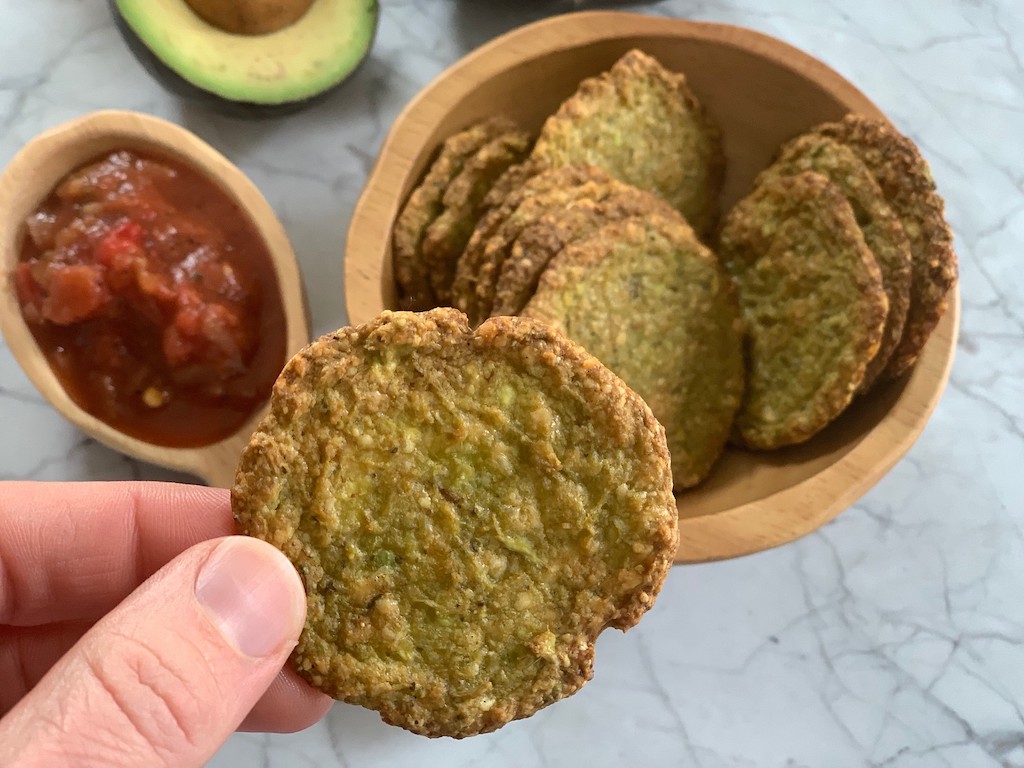 keto game day snacks - hand holding a round avocado chip with bowl and salsa in background
