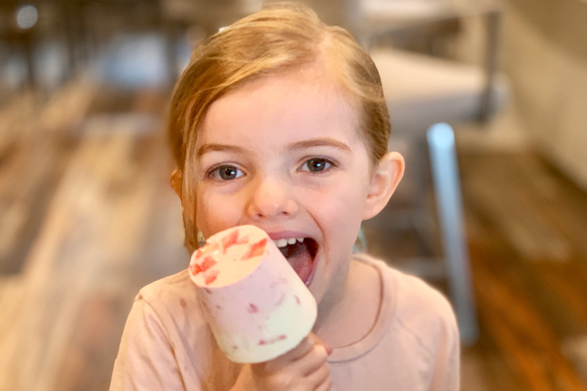a young girl licking a keto strawberry cheesecake popsicle