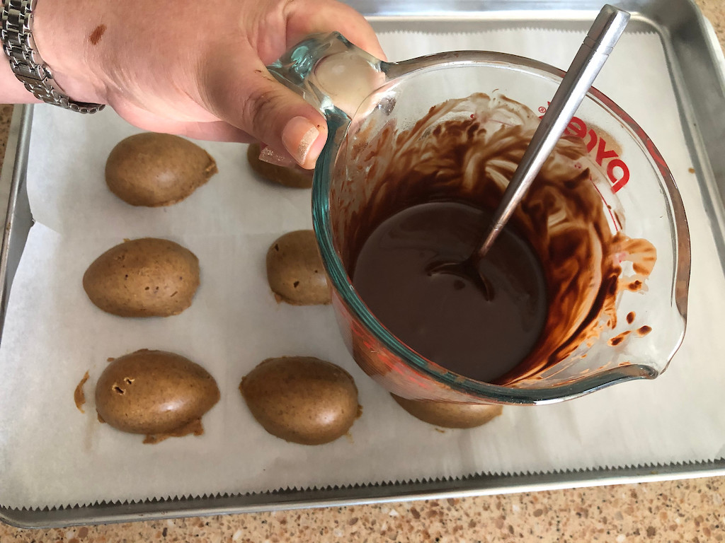 peanut butter eggs on pan with melted chocolate in glass measuring cup