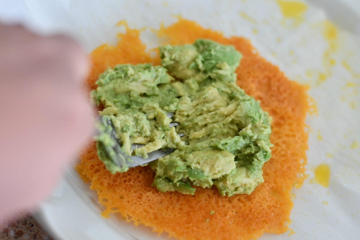 spreading mashed avocado on a microwaved piece of cheese 