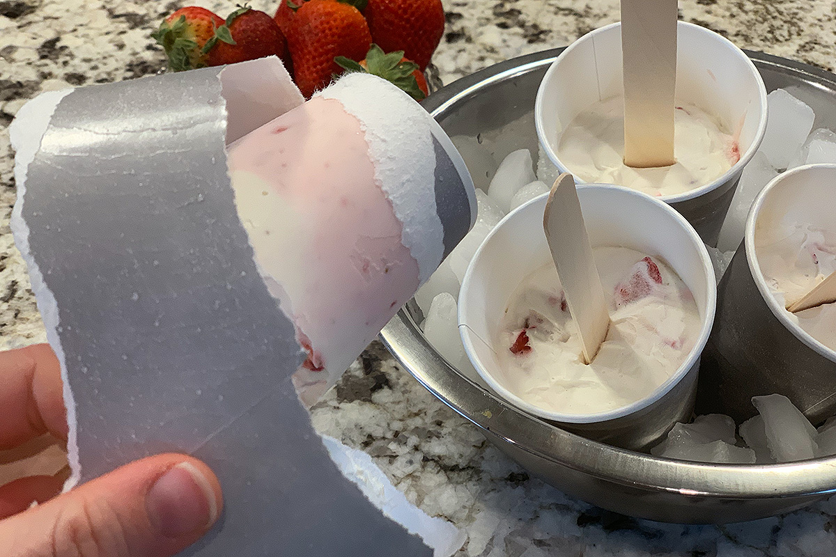 a dixie cup being torn off a strawberry cheesecake popsicle