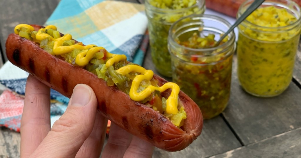 holding hot dog with relish and mustard 