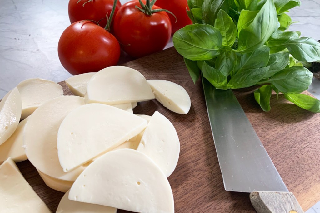 a cutting board with tomatoes, basil, and freshly sliced mozzarella