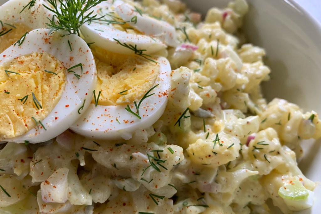 a close-up view of keto cauliflower potato salad garnished with sliced egg