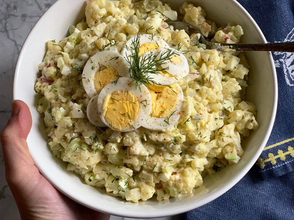 a person serving a bowl of low-carb cauliflower no-potato salad