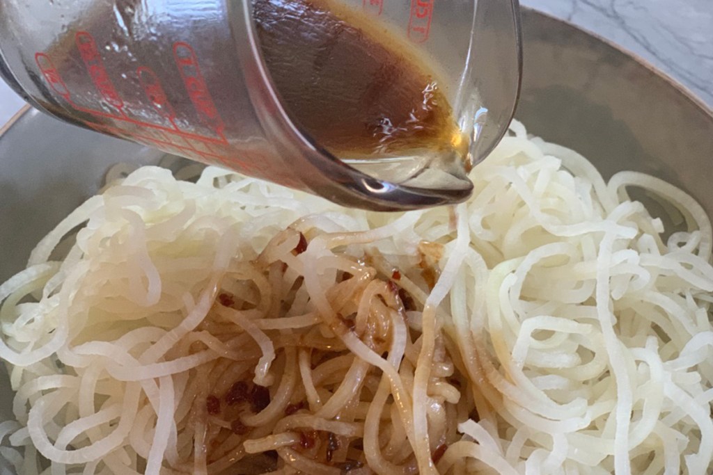 sesame marinade being poured over daikon radish noodles 