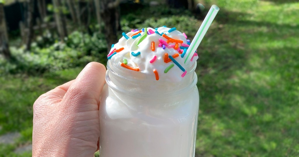 a hand holding a glass of birthday cake shake
