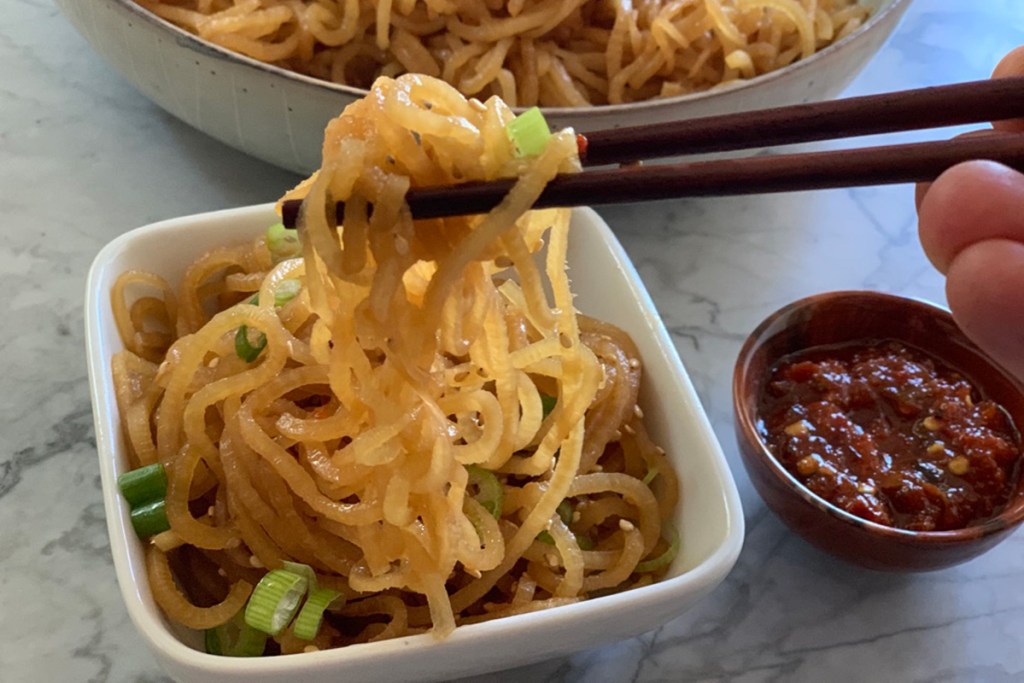 Palillos recogiendo un gran bocado de fideos de sésamo