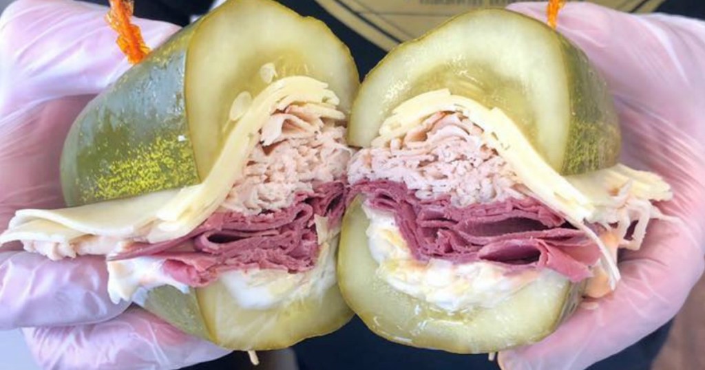 holding a pickle sandwich with turkey and cheese