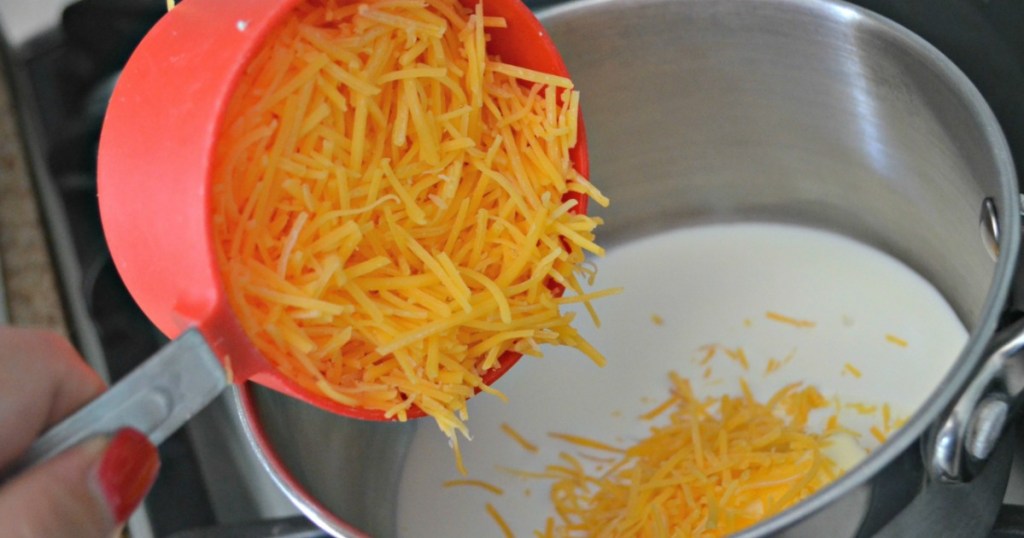 shredded cheese being dumped into saucepan with cream