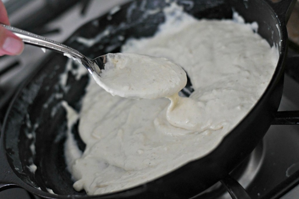 spoon of homemade keto alfredo sauce in a skillet 