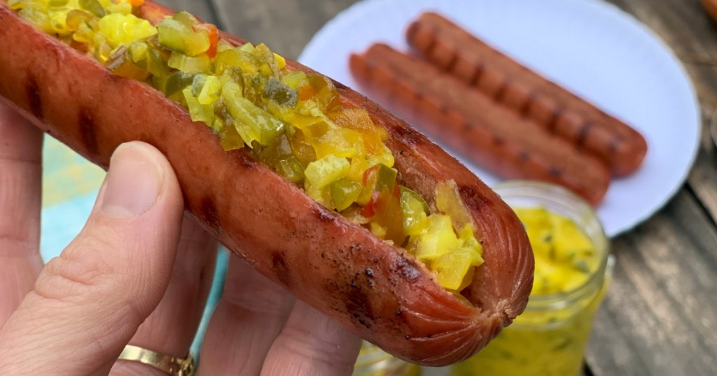 holding sliced hot dog filled with relish 