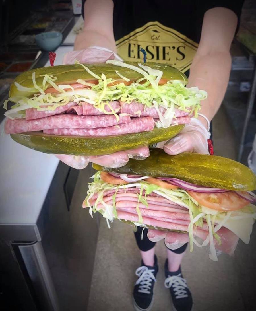 holding two large pickle sandwiches filled with meat and veggies 
