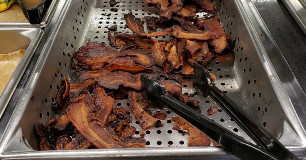 cooked bacon in serving tray with black tongs 