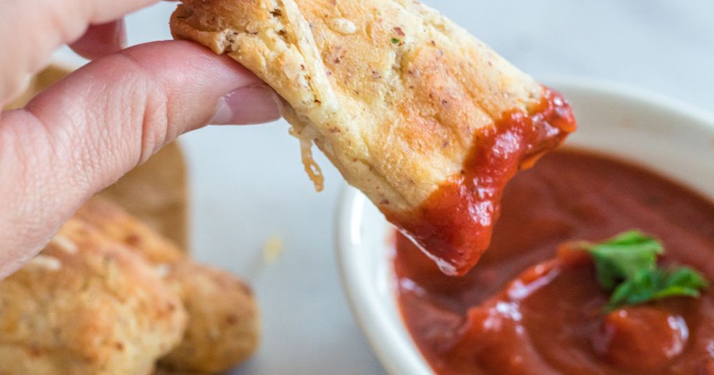 dipping keto breadsticks into marinara sauce 