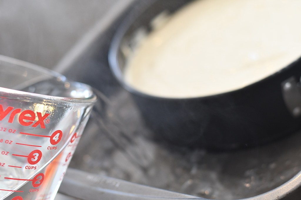 pouring water into pan to keto cheesecake water bath before baking