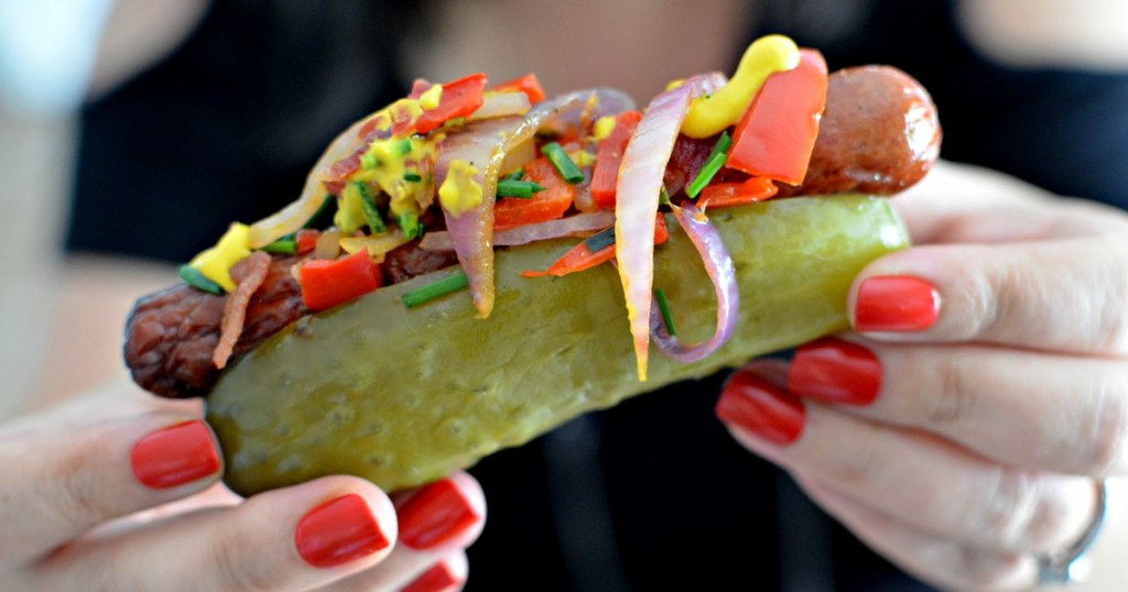 holding a pickle hot dog loaded with condiments