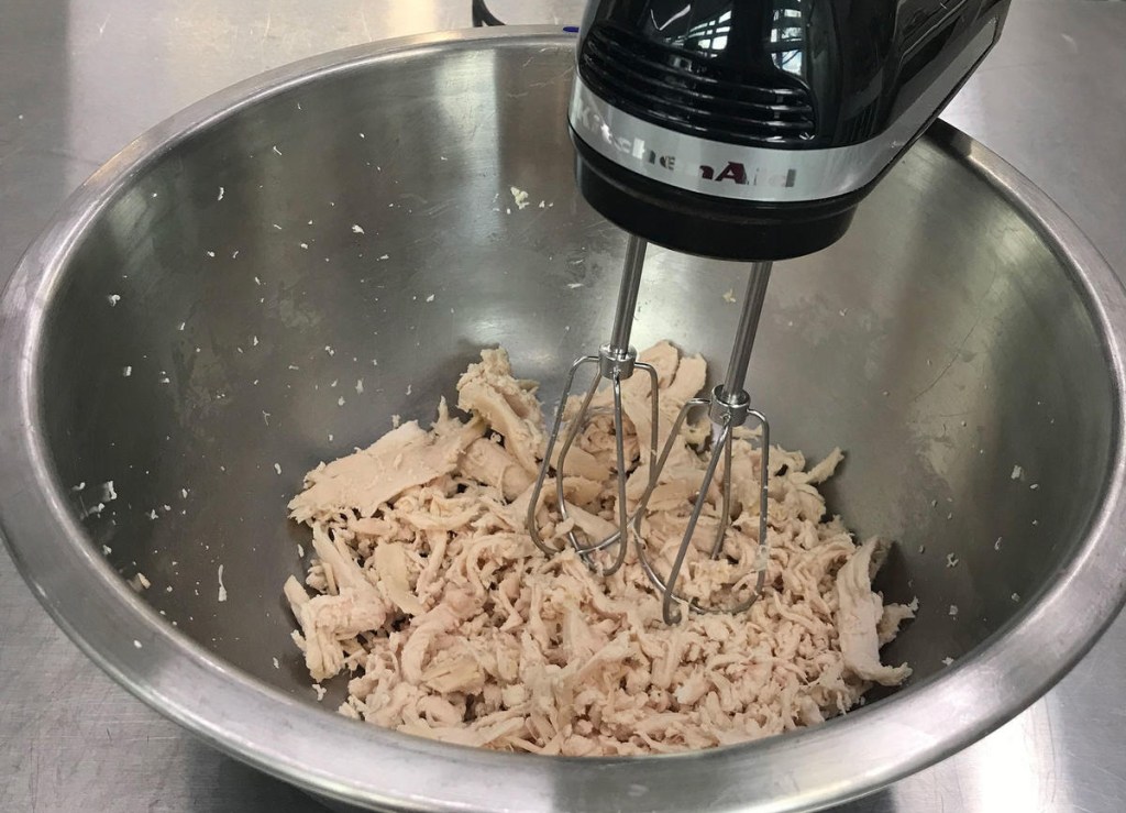 kitchenaid hand mixer beating chicken into shredded pieces