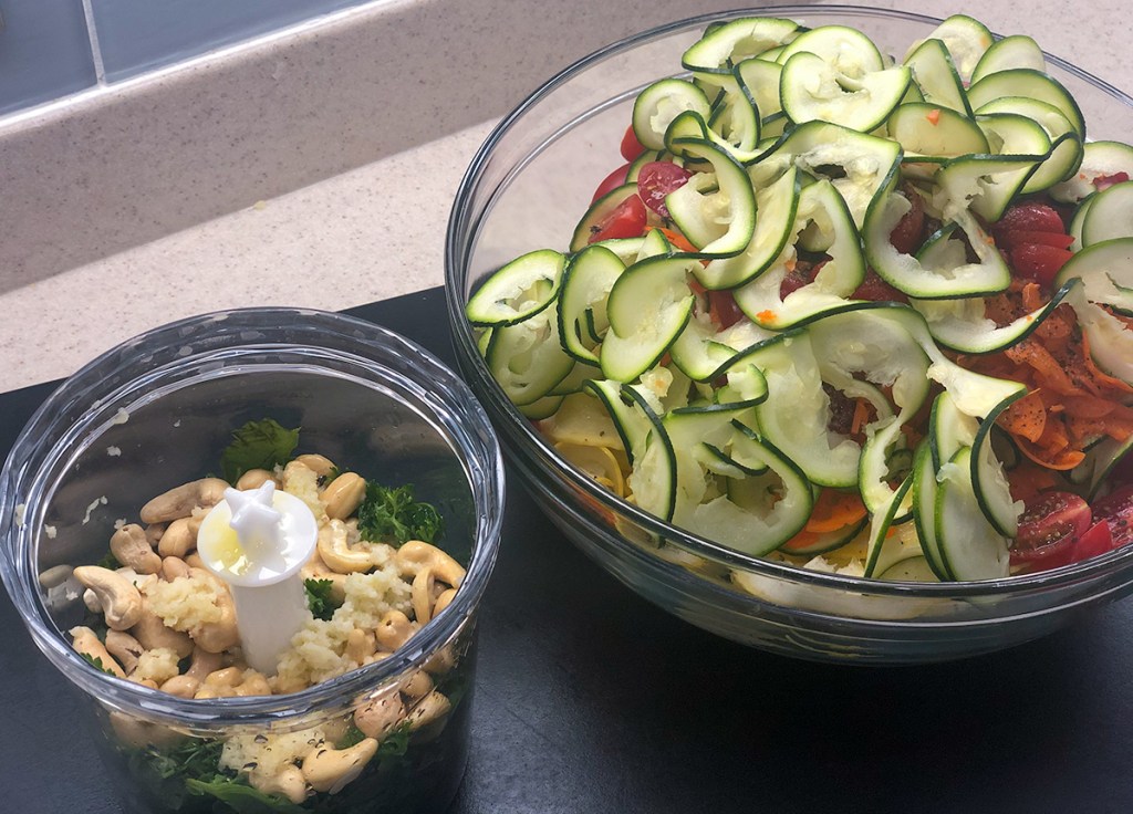 bowl of spiralized zucchini and pesto ingredients in food processor