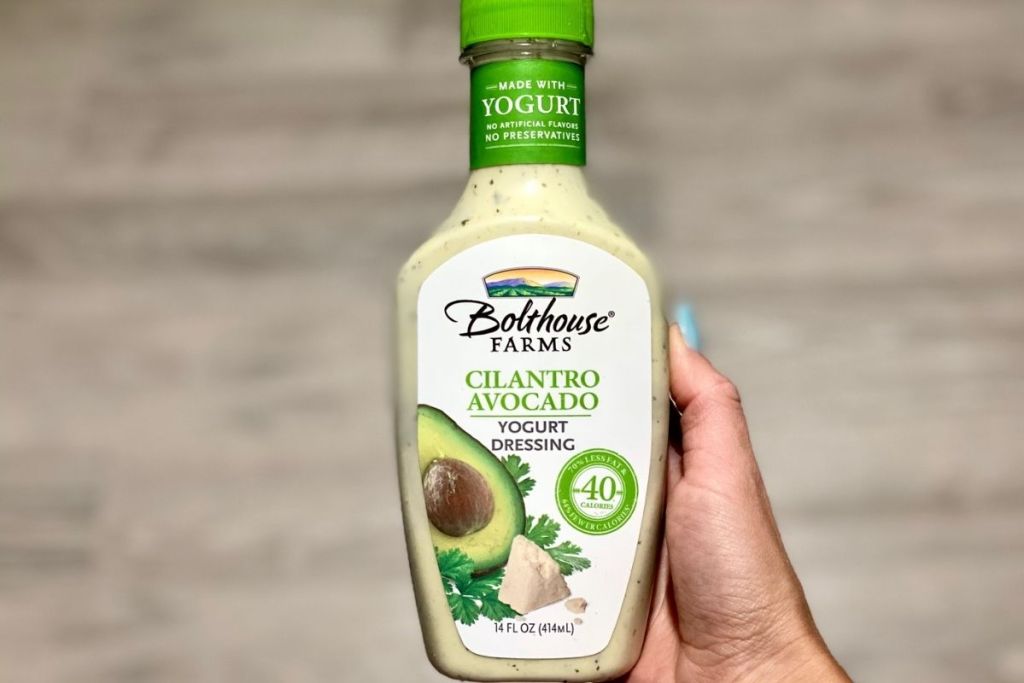 A hand holding a bottle of cilantro avocado salad dressing