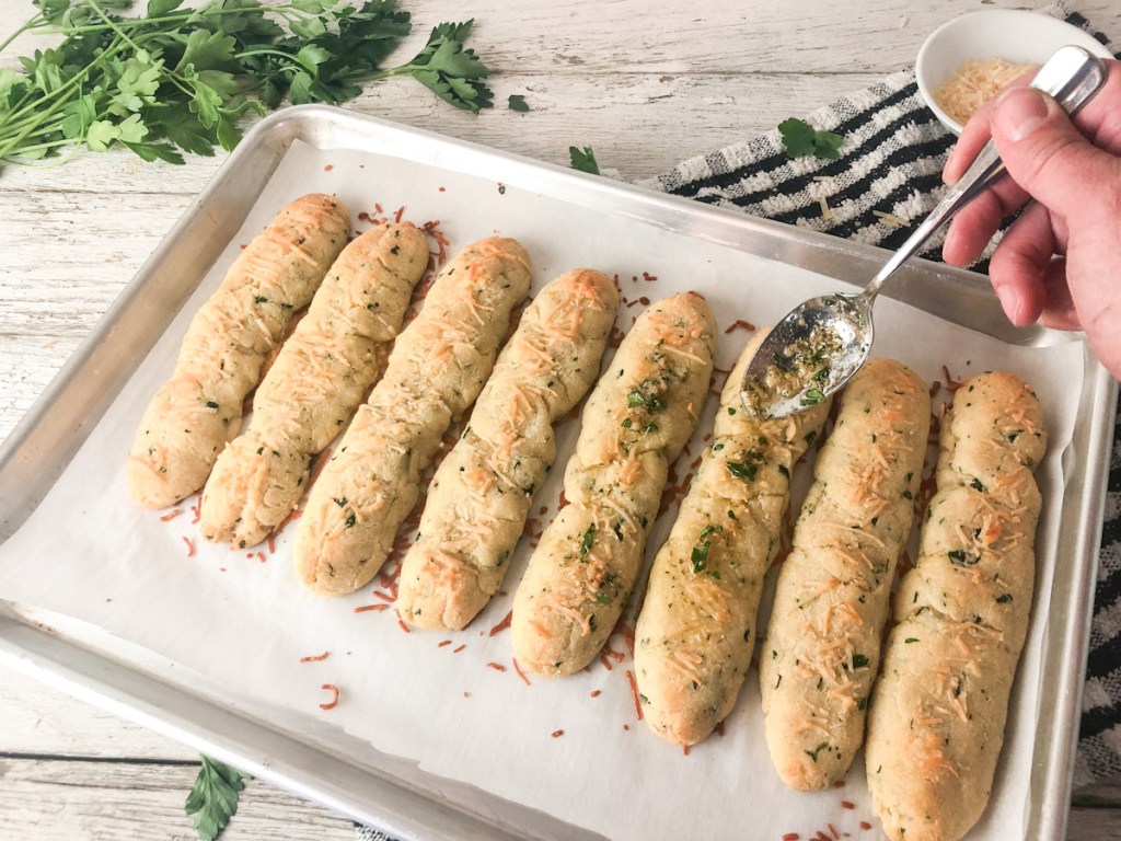 spreading butter herb mixture on baked breadsticks