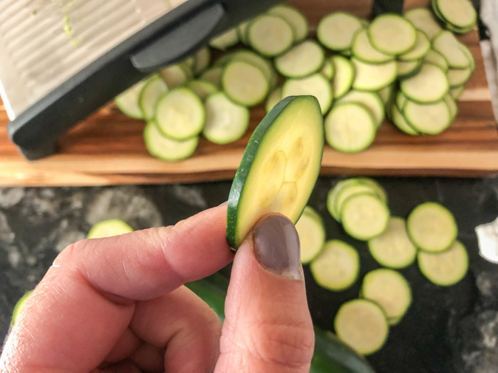 holding up a thin slice of zucchini