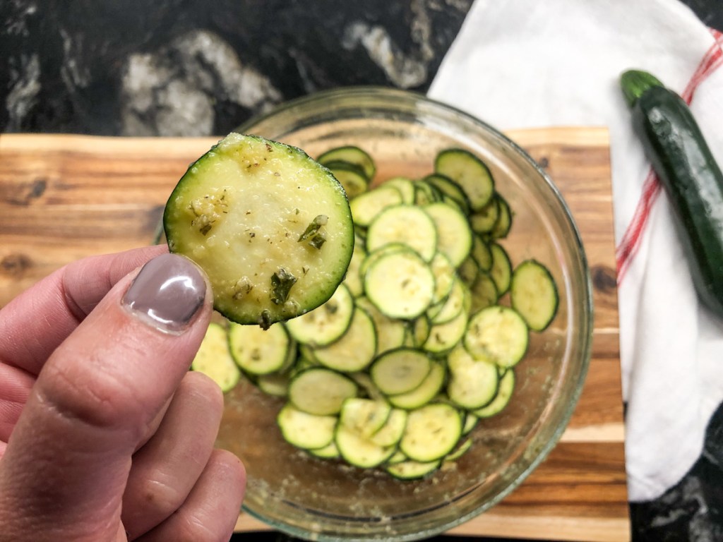 holding a zucchini slice with seasoning on it