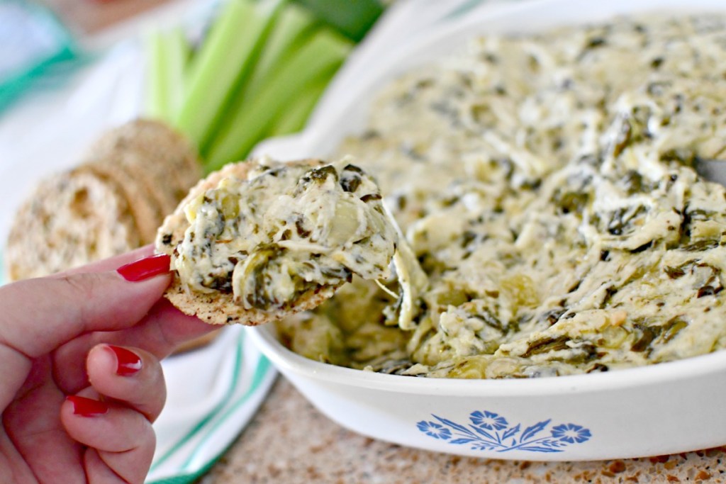 dipping a parmesan crisp into artichoke dip