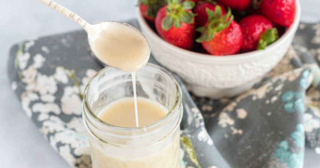 spoonful of spoonful of homemade condensed milk with a bowl of strawberries