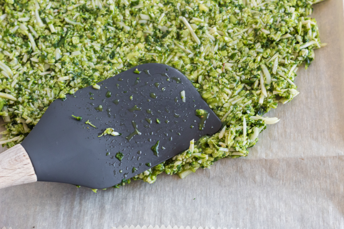 flattening out a broccoli pizza crust with spatula 