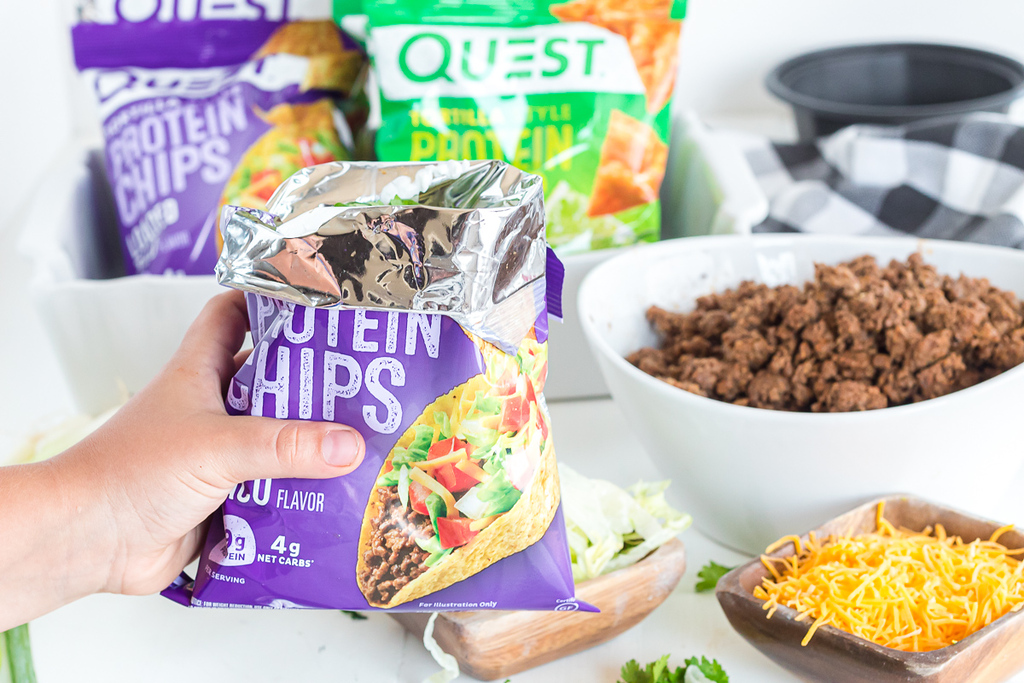 holding Quest chips bag with taco toppings around it