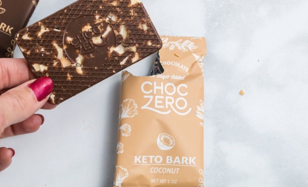 A hand holding a piece of keto bark next to the wrapper