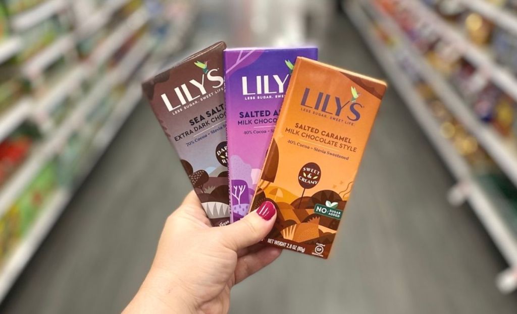 A hand holding Lily's chocolate bars at a store