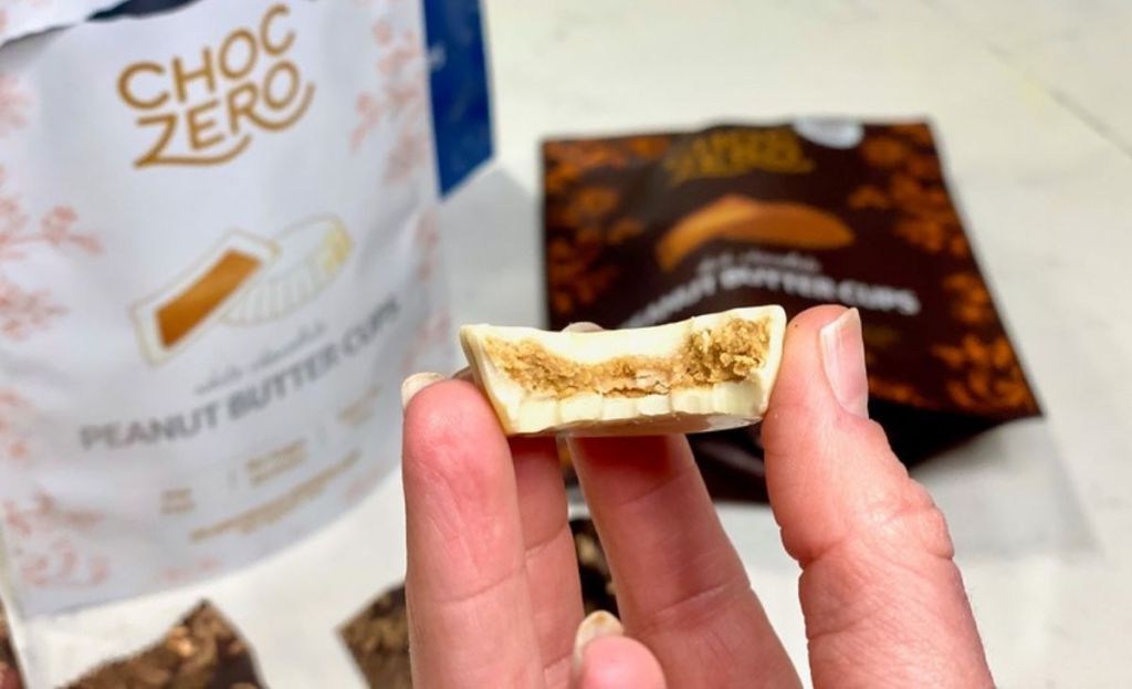 A hand holding a white chocolate peanut butter cup with a bite out of it