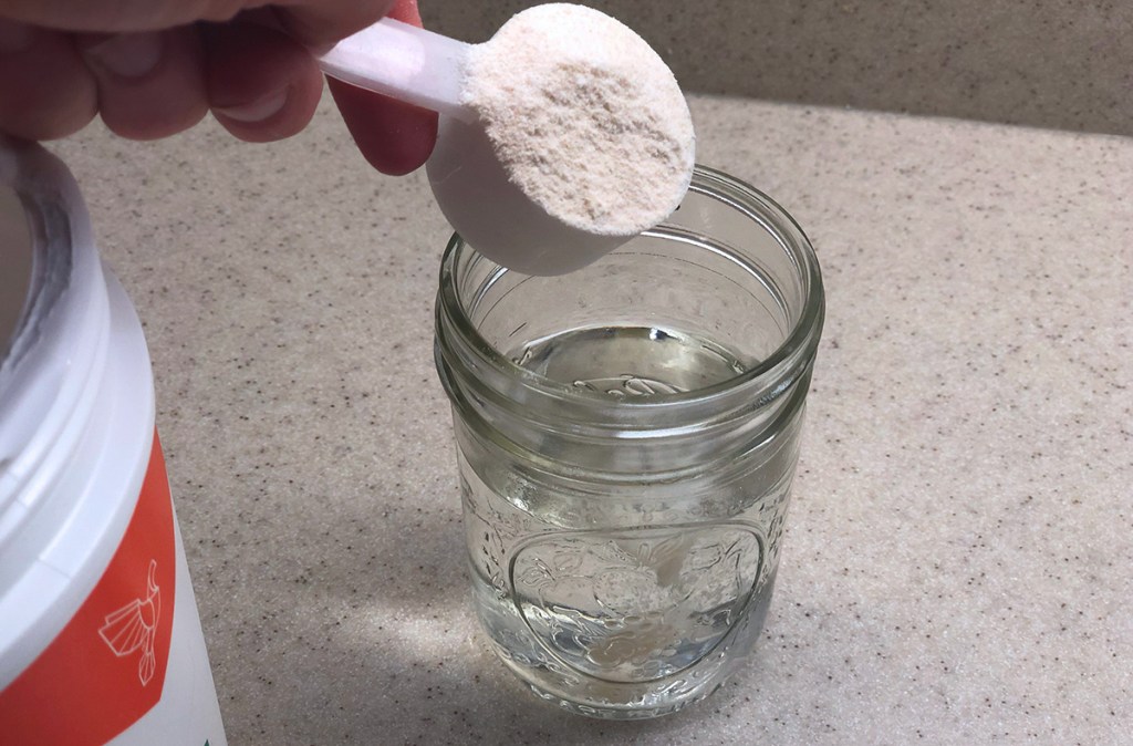 Scooping Bulletproof InnerFuel Prebiotic powder into glass of water