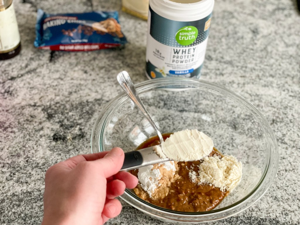 adding protein powder to almond butter in a mixing bowl