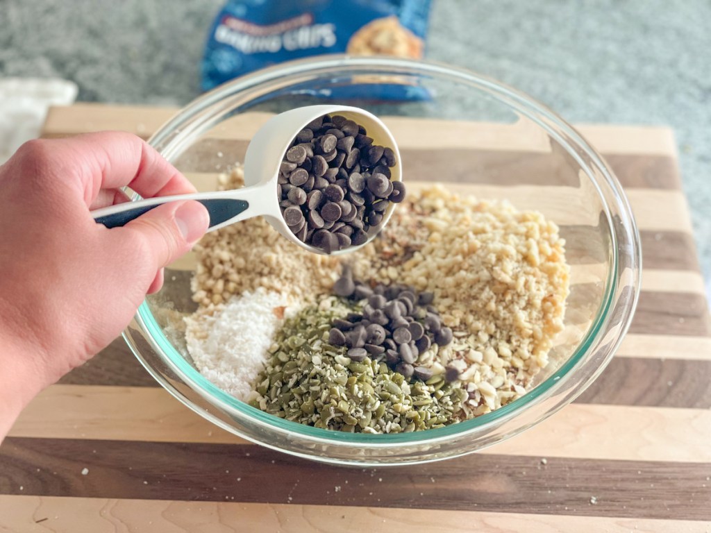 adding keto chocolate chips to a bowl with nuts