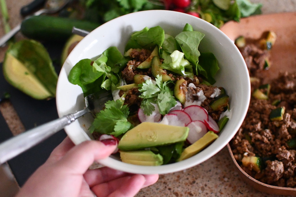 holding white bowl with beef taco salad inside 