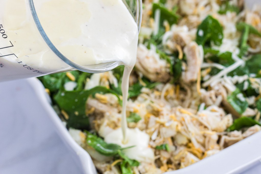 pouring Alfredo sauce over casserole