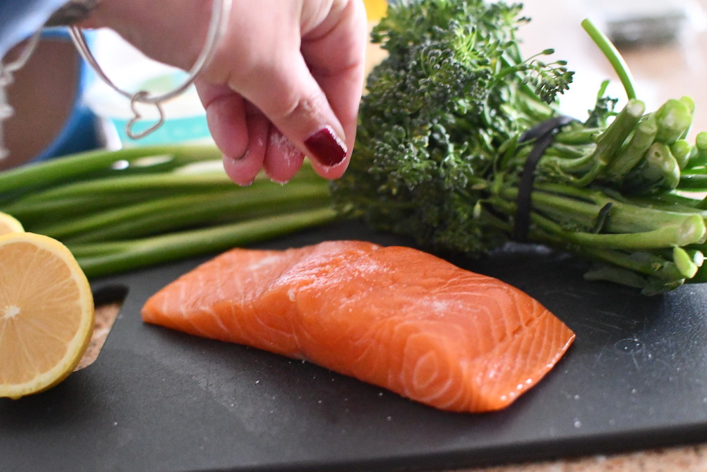 salting salmon on black cutting board with broccoli