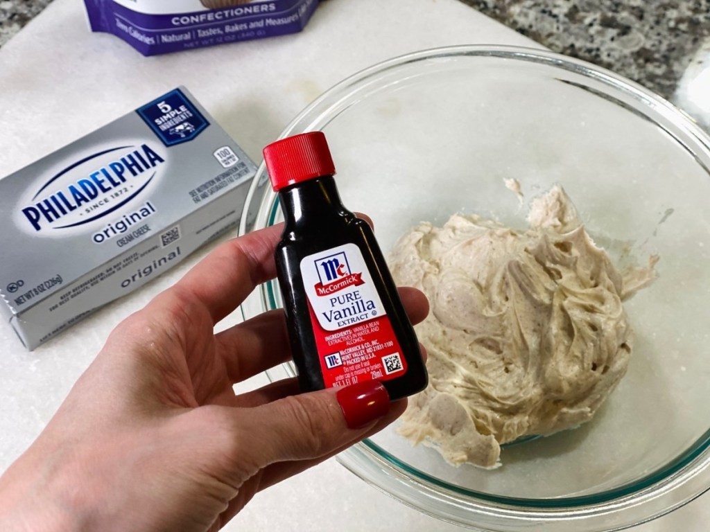 hand holding bottle of vanilla over cream cheese frosting in bowl