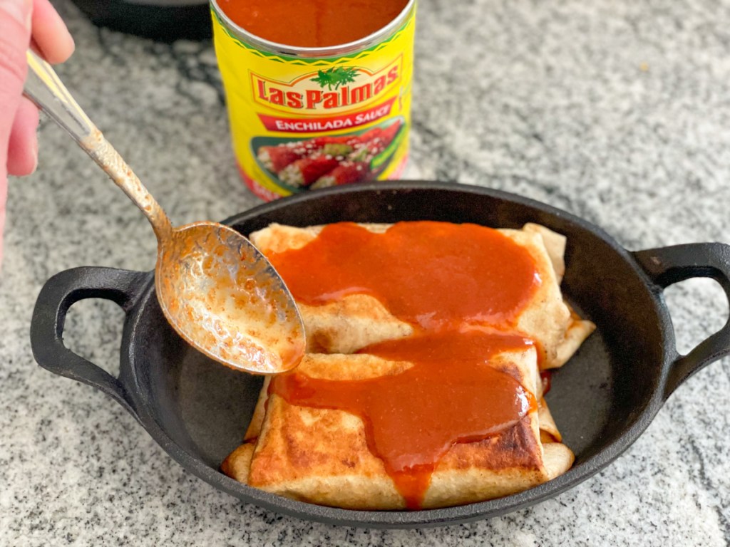 adding enchilada sauce to burritos