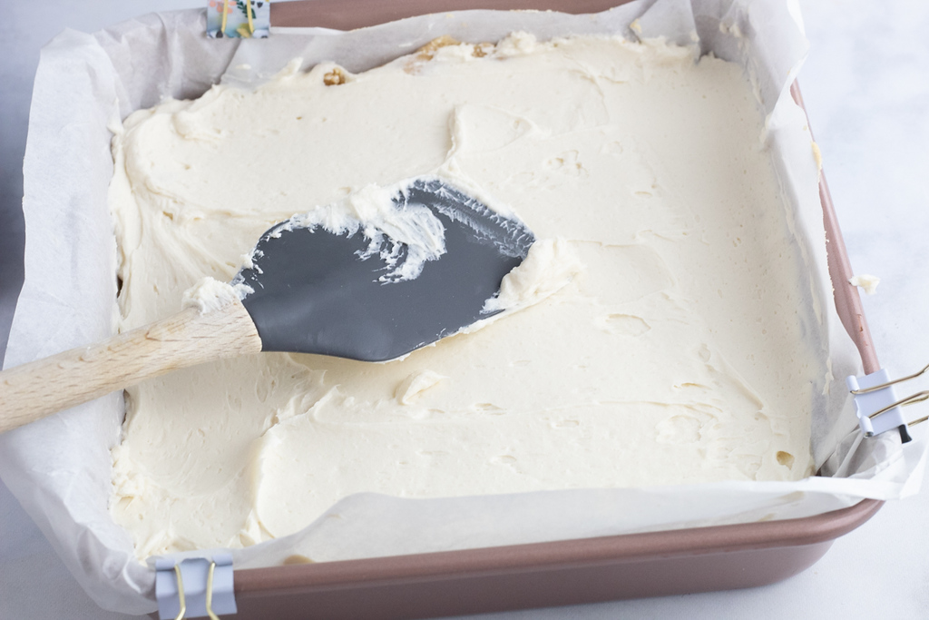 spreading sweet cream cheesewith spatula in casserole dish 