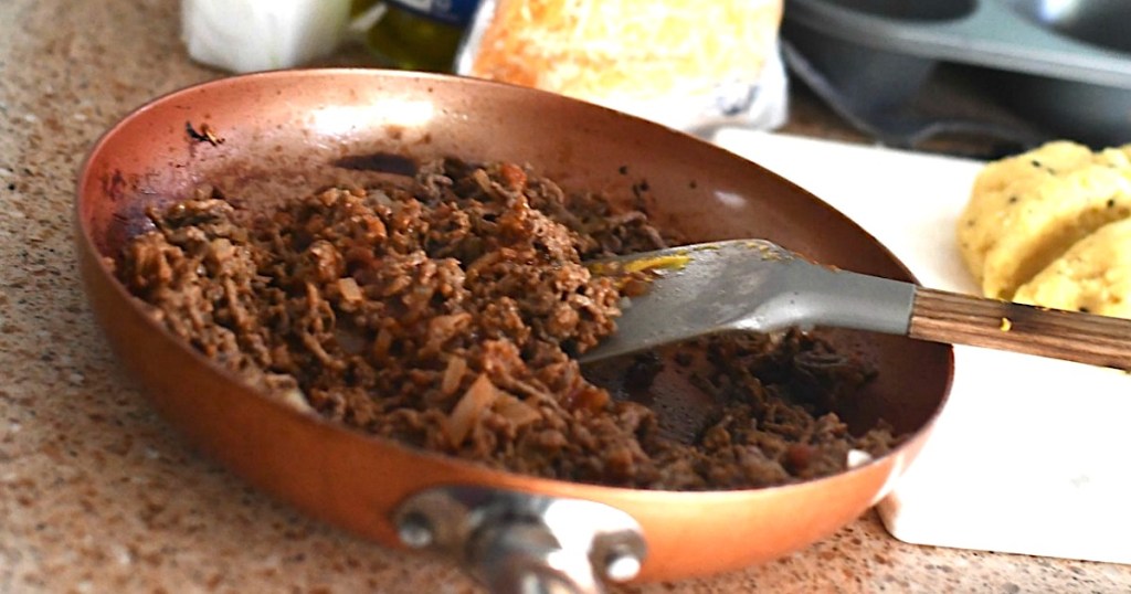 copper pan with ground beef inside and metal spatula 