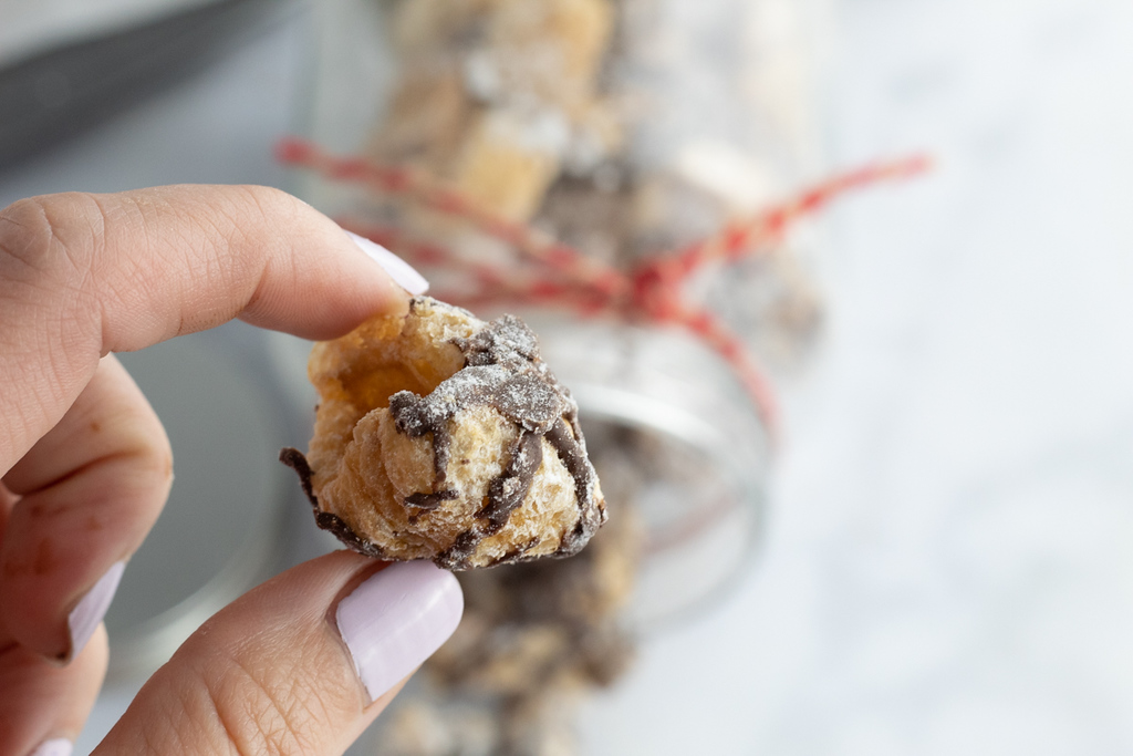 holding piece of chocolate drizzled keto puppy chow 